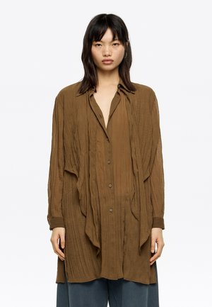 Camicia button-up marrone con un design drappeggiato, maniche lunghe e colletto. Leggermente oversize con una vestibilità rilassata.