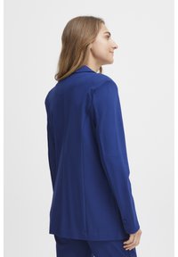 Modrý štruktúrovaný blazer s výstrihom do V, prispôsobeným strihom a hladkou textúrou. Obsahuje manžety na jedno gombík a čistý, elegantný dizajn chrbta.