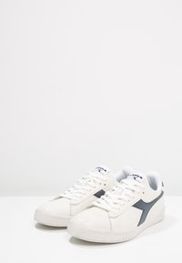 Vita lädersneakers med en strukturerad finish. Har en mörkblå accent och perforerade sidor. Inkluderar platta snören och en gummisula.
