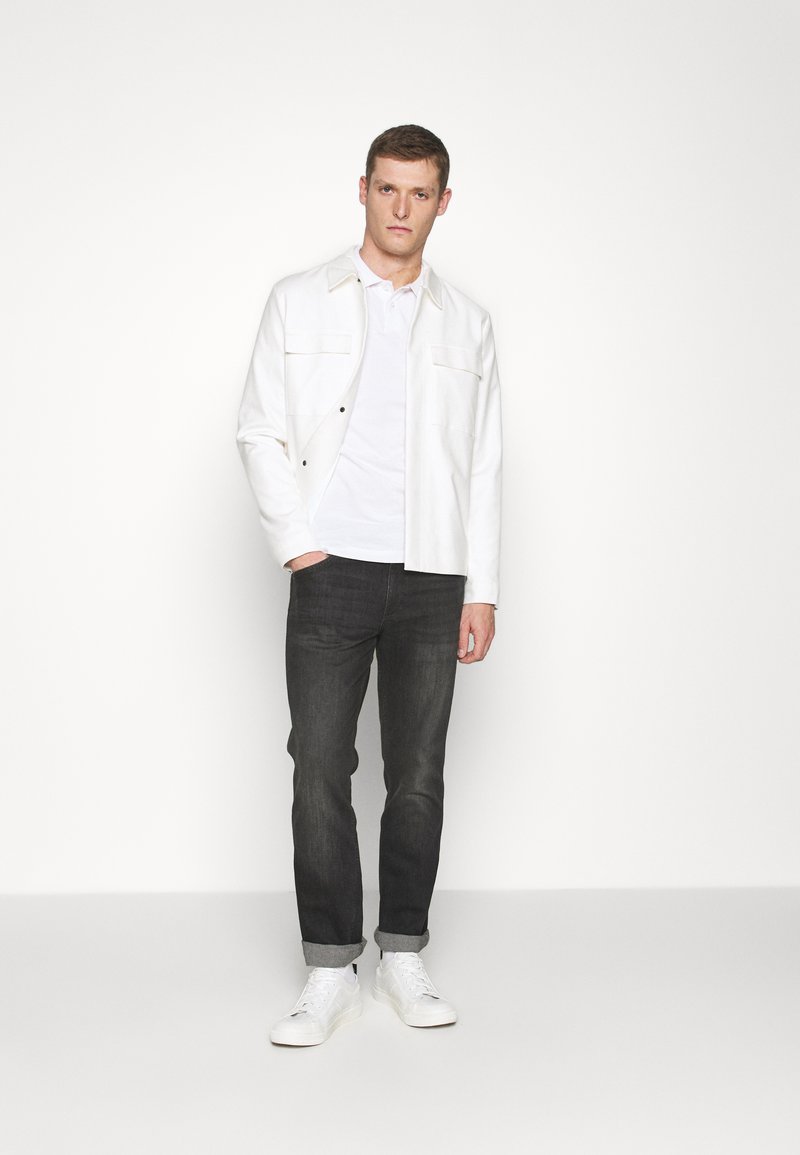 Hvit jakke over en hvit t-skjorte, paret med mørke jeans og hvite sneakers. Jakken har to brystlommer og et rent design.