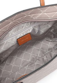 Šedá látková taška s texturovaným povrchem, uvnitř s béžovou podšívkou s vzorem kruhů a čar, a hnědá kožená visačka.