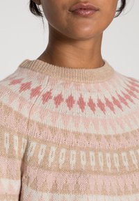 Stickad tröja med en mjuk textur, med rund halsringning. Mönster i ljusrosa, beige och vitt, med geometriska diamantformer.