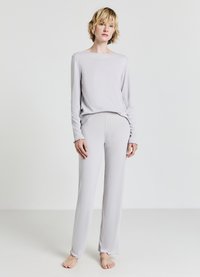 Ensemble de loungewear gris clair en tissu doux et texturé. Haut à manches longues avec un col rond ; le pantalon présente des ourlets effilochés.