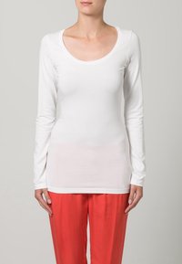 Witte katoenen top met lange mouwen en een ronde hals, met een aansluitend ontwerp en een gladde textuur, gecombineerd met losse rode broeken.
