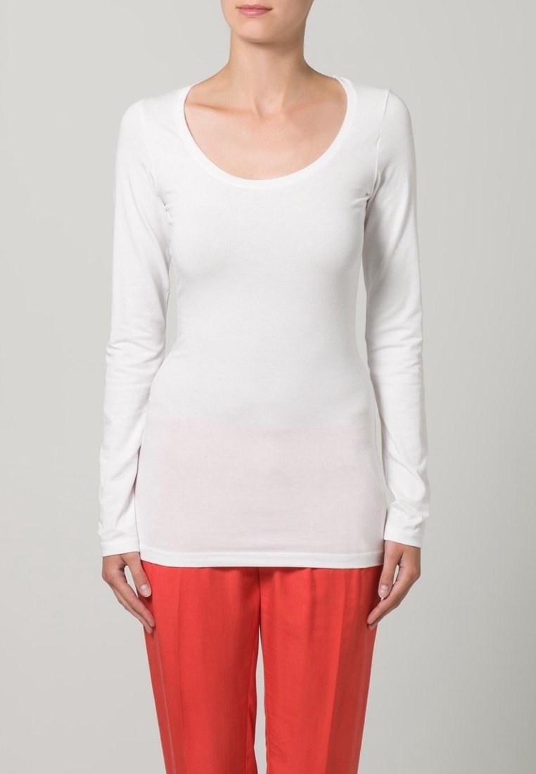 Witte katoenen top met lange mouwen en een ronde hals, met een aansluitend ontwerp en een gladde textuur, gecombineerd met losse rode broeken.