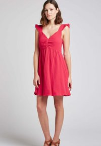 Robe en coton rouge avec un décolleté en V, des manches courtes à volants et un corsage ajusté. La jupe s'évase légèrement pour un ajustement décontracté.