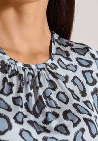 Lichtblauwe blouse met zwart en grijs luipaardprint. Zachte stof, ronde halslijn en geplooid detail bij de hals.