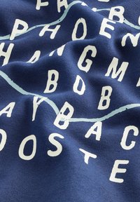Tessuto blu navy con scritte bianche disposte in un modello casuale. Morbida texture con un aspetto informale e rilassato. Accenti azzurri chiari visibili.