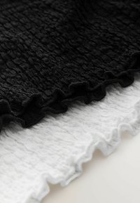 Zwart-witte stof met een gekreukte textuur en gerimpelde randen. Het zwarte materiaal ligt bovenop een witte achtergrond.