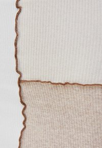 Pružná textilie se štěpeným designem; jedna strana je krémová s hnědým vlnitým švem, druhá strana je světle taupe s podobným vzorem.