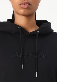 Zwarte hooded sweatshirt met een buidelzak, voorzien van een reliëf "Calvin Klein" logo in bijpassende draad en verstelbare koorden met zilveren hardware.