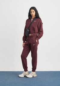 Bordeaux-coloured collegehousut ja matchaava lyhyt huppari vetoketjulla, jossa on Nike-logo. Yhdistettyinä vaaleisiin tennareihin ja pieneen mustaan olkalaukkuun.