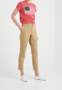 Červené tričko s grafikou americké vlajky. Béžové upravené kalhoty. Bílé tenisky. Jednoduchý, neformální outfit s čistými liniemi.