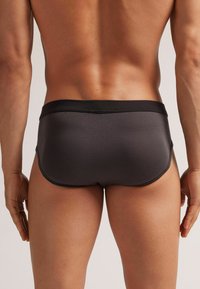 Herren graue Badebriefe mit einem schwarzen elastischen Bund. Glattes, dehnbares Material passt sich eng der Körperform an und zeichnet sich durch ein minimalistisches Design aus.