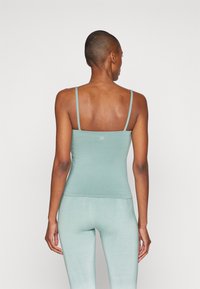 Light teal tank top with thin straps, smooth texture, fitted design, and a small logo on the back. Paired with matching fitted leggings.