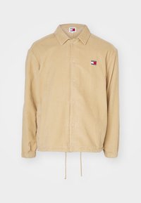 Béžová kordurová bunda s knoflíkovým zapínáním, upraveným límcem a stahovacími lemy. Obsahuje malé logo Tommy Hilfiger na hrudi.