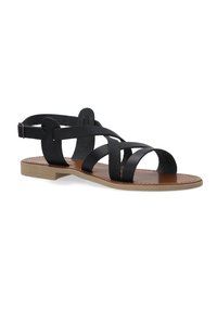 Schwarze Lederflachsandalen mit überkreuzten Riemen und einem hinteren Knöchelriemen. Hochschuh hat ein braunes Lederfußbett und eine hellbraune Sohle.