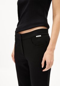 Zwarte stretchbroeken met een gladde textuur, voorzien van een aansluitende taille, zijzakken en een klein label op de tailleband.