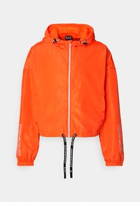 Lyst orange kort jakke med hætte, lavet af glat stof. Har sorte snore og hvid logo tekst på ærmerne og lynlåsen.