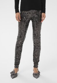 Črne legice okrašene s sequini, z prilagojeno zasnovo, ki vključuje teksturirane vzorce in elastične manšete. Nosi se z sivimi nizkimi čevlji s vozlom.