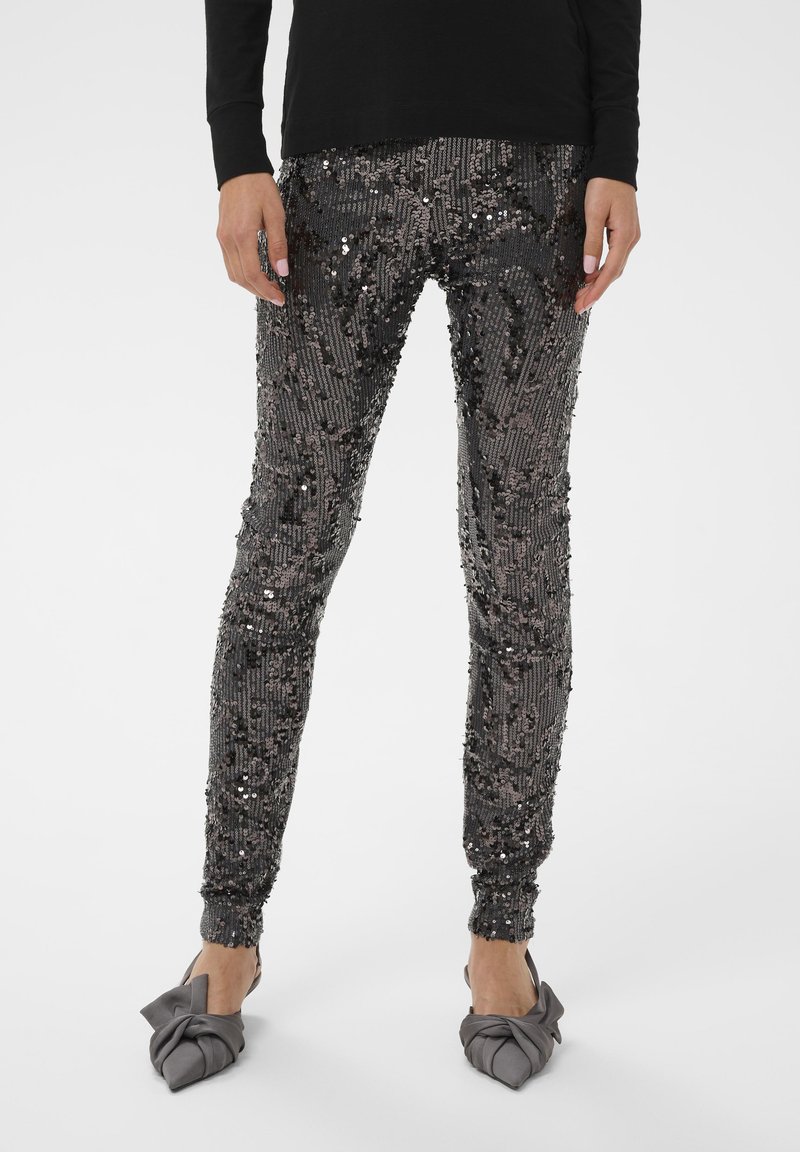 Črne legice okrašene s sequini, z prilagojeno zasnovo, ki vključuje teksturirane vzorce in elastične manšete. Nosi se z sivimi nizkimi čevlji s vozlom.