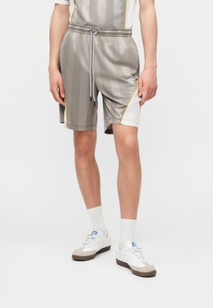 Άνδρας που φοράει γκρι ριγέ αθλητικό σορτς με λευκές και κίτρινες πλευρικές πινελιές, λευκές κάλτσες και λευκά αθλητικά παπούτσια με μπλε λογότυπο.