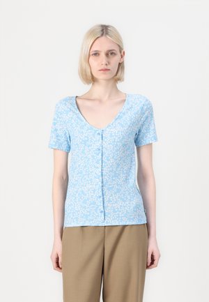 Blue short-sleeve button-up top with a v-neckline, featuring a floral pattern and a ribbed texture, paired with light brown trousers.