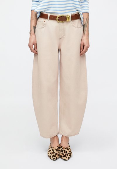 Pantalon beige à jambes larges avec poches latérales, associé à une ceinture marron à boucle dorée et des mules à imprimé léopard. Texture du tissu lisse.