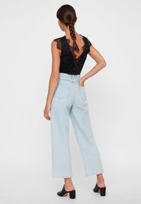 Body in pizzo nero con scollatura a V e maniche a cappuccio, abbinato a jeans wide-leg a vita alta di colore blu chiaro. Mules neri con tacco completano il look.