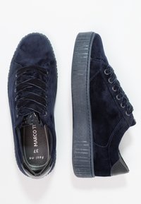 Námořnické modré semišové tenisky s texturovanou gumovou podrážkou, kulatou špičkou a šněrovacím designem. Obsahují lesklé černé akcenty na patě a jazyku.