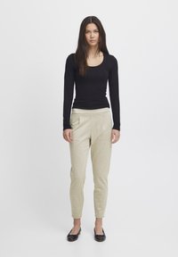Black long-sleeve top with a scoop neckline, paired with beige checkered trousers featuring side pockets and tapered legs. Black flats complete the look.
