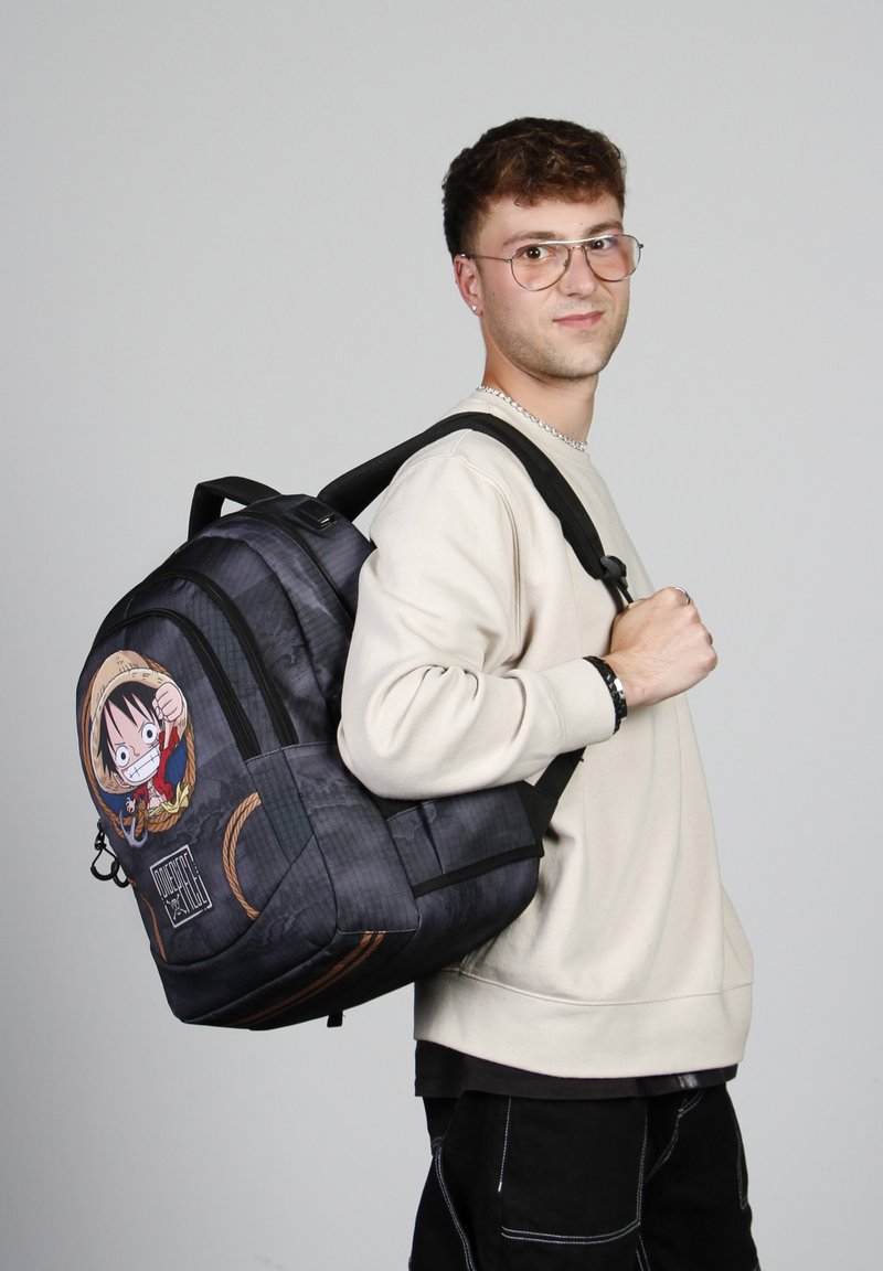 Mochila de tela negra con diseño de personaje, que presenta una figura de dibujos animados en la parte frontal. Correas ajustables y detalles en la superficie texturizada.