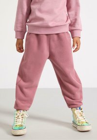 Vaatteet, johon kuuluu rentomalliset vaaleanpunaiset fleece-housut, joissa on ribbetyt hihnat ja pieni logo. Yhdistetty sateenkaarenvärisiin korkeisiin tennareihin.