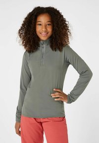 Langsleeve, hooggezoomd shirt van olijfgroene stof met een halve ritssluiting aan de voorkant en platlock naden, gecombineerd met koraalkleurige broeken.
