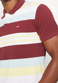Poloko s krátkým rukávem pruhované v barvách maroon a světle modré, s límečkem a malým červeným logem Levi's na hrudi. Měkká textura.