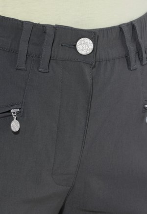 Nahaufnahme von dunkelgrauen Hosen mit Gürtelschlaufen, Reißverschlusstasche und einem silbernen Knopf mit eingraviertem Text.