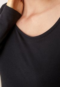 Svart långärmad tröja med rund halsringning, tillverkad av slätt tyg med en figursydd silhuett och noggranna sömmar längs halsringningen.