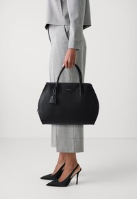 Czarna skórzana torebka o textured powierzchni, charakteryzująca się wyraźnym kształtem, górnymi uchwytami oraz małym detalem w postaci frędzla.