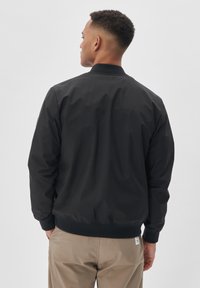 Must nahktagi ribidega krae ja mansettidega, valmistatud siledast materjalist. Omab lõdvestunud istuvust ja on kombineeritud helekaki pükstega.