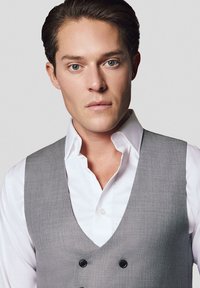 Szary kamizelka na białej koszuli, z klapami i podwójnymi guzikami. Gładki materiał o subtelnym wzorze; dopasowany krój.