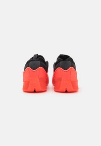 Fekete és élénkpiros sportcipők párnázott talppal, textil felső résszel, sarok támogatással és hurkkal a könnyű felhúzáshoz. Hátsó nézetben hangsúlyos forma látható.