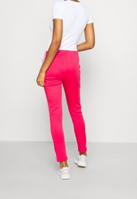 Růžové tepláky s bílými postranními pruhy; elastický pas, slim fit a jemná textura, spárované s bílým topem s krátkým rukávem a bílými teniskami.