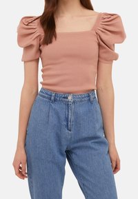 Light pink ribbed sweater with square neckline and puffed sleeves, paired with high-waisted blue denim jeans featuring a floral button.