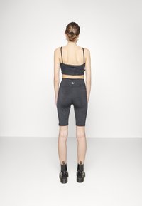 Černá sportovní podprsenka a vysoké cyklistické šortky s texturovaným vzorem, doplněné černými kotníkovými botami. Pohled zezadu na jednobarevném pozadí.