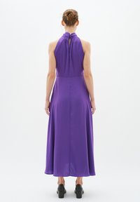 Rochie maxi fără sleeves de culoare mov, cu guler halter și un design cu tăietură în spate. Fabricată dintr-un material neted, cu o siluetă fluidă. Pantofi negri cu toc bloc.