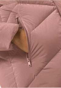 Ręka w niezapinanej kieszeni różowej pikowanej kurtki o przekątnym przeszyciu.