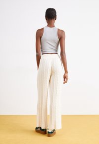 Krämtvättade creamfärgade byxor med kabelmönster, hög midja och vida ben. Matchas med tealfärgade plattformssandaler och en grå crop top.