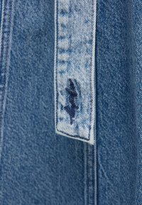 Jeansjacke mit fransigem Saum in hellblau. Verfügt über einen abgenutzten Patch mit dunkelblauen Nähten an den Bündchen. Die Textur ist weich und strukturiert.
