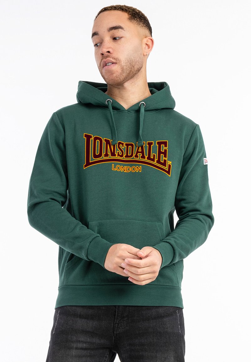 Zelena dukserica od pamuka s prednjim kengurujem džepom i užetom. Ima veliki žuti i crveni Lonsdale London logo na prsima.