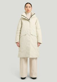 Ljusbeige isolerad kappa med hög krage, framknäppning och vida ärmar. Passar bra med gräddfärgade byxor och svarta skor.